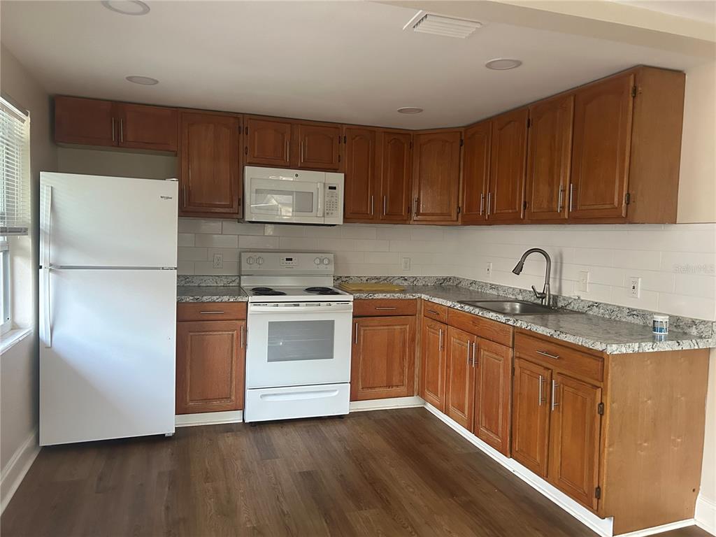 A kitchen features wood cabinets, white appliances, granite countertops, and a white subway tile backsplash — 2824 MEADOW VIEW AVENUE, LARGO, FL