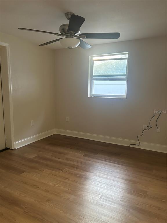 An empty room features light wood-look flooring, beige walls, a ceiling fan, and a window — 2824 MEADOW VIEW AVENUE, LARGO, FL