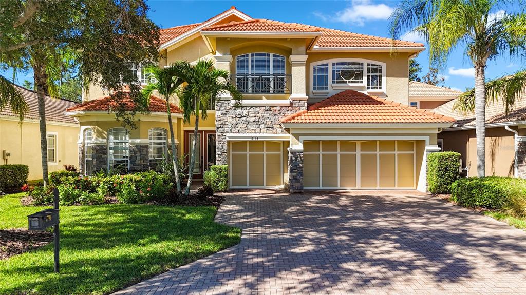 A two-story house with a tiled roof, stone accents, and a paved driveway — 8134 SANTA ROSA COURT, SARASOTA, FL