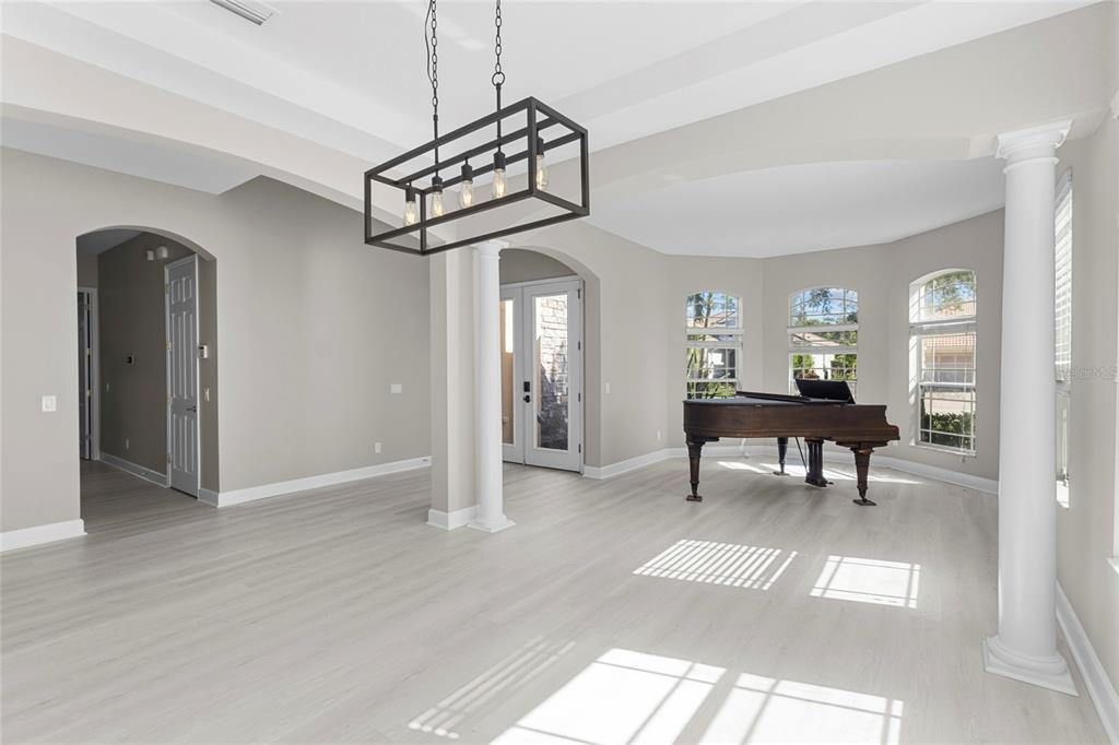 A bright living area features light wood flooring, a grand piano, and a rectangular pendant light — 8134 SANTA ROSA COURT, SARASOTA, FL