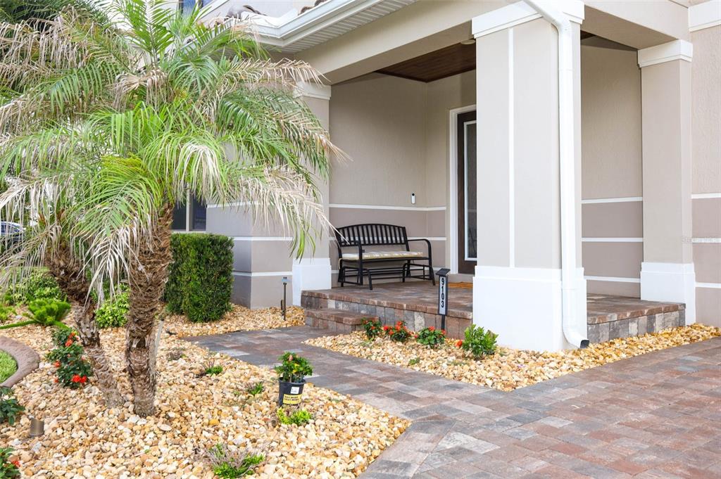A paved walkway leads to a covered front porch with a bench and palm tree — 9103 MORGANA COURT, WINTER GARDEN, FL
