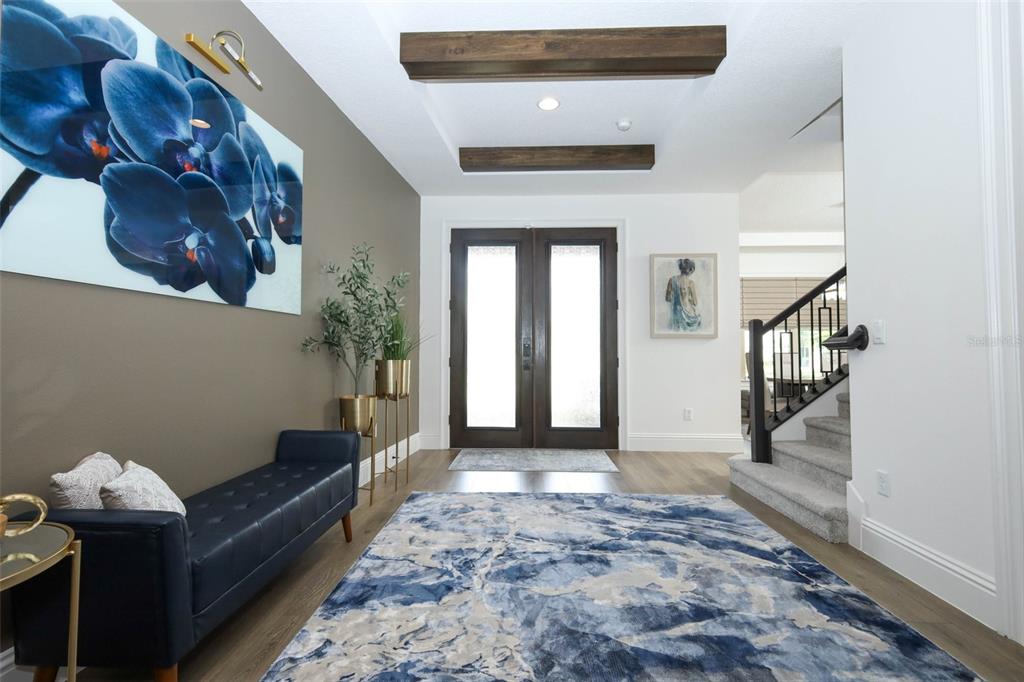A modern entryway features a blue rug, a leather bench, and dark wood ceiling beams — 9103 MORGANA COURT, WINTER GARDEN, FL