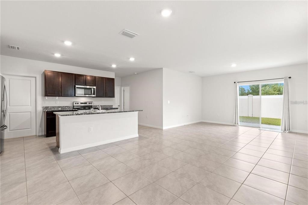 An open-concept kitchen with dark cabinets and a granite island flows into a living area — 3226 SUNCOAST PLAINS DRIVE, ODESSA, FL
