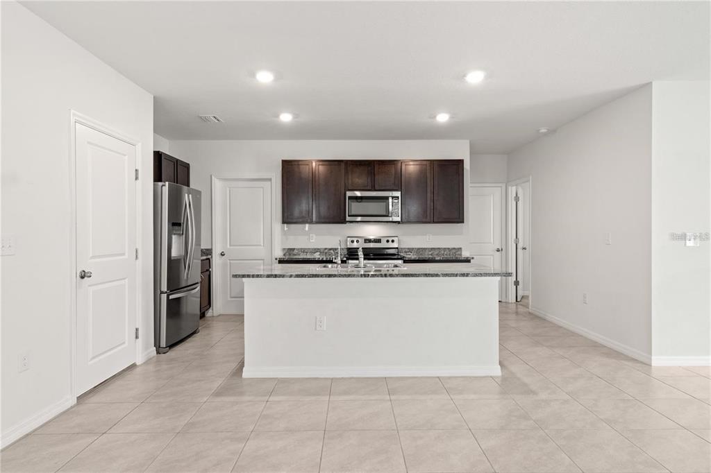 A kitchen features dark wood cabinets, stainless steel appliances, a granite island, and tile flooring — 3226 SUNCOAST PLAINS DRIVE, ODESSA, FL
