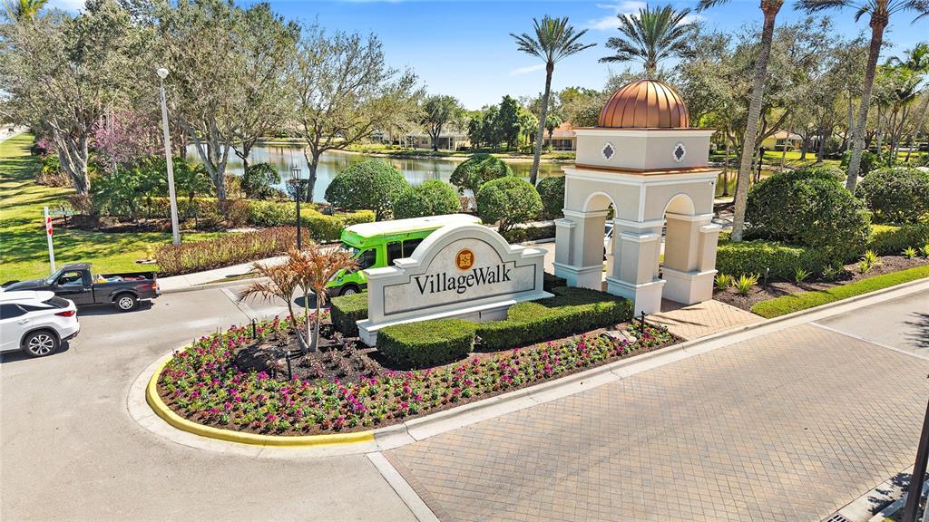 An exterior view of the VillageWalk community entrance featuring a sign, landscaping, and a pond — 15127 REEF LANE, BONITA SPRINGS, FL