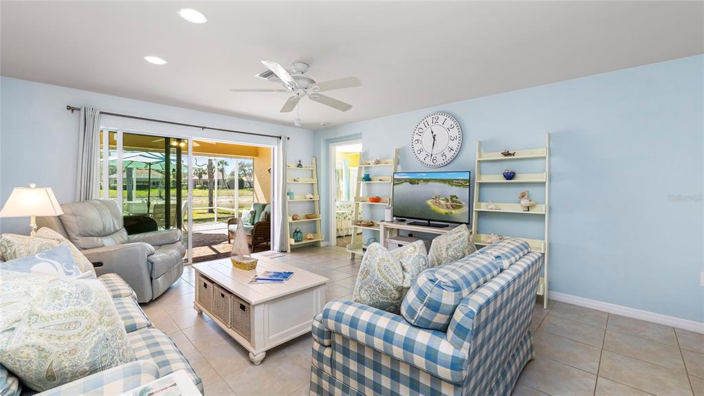 A living room features light blue walls, a plaid sofa, a television, and sliding glass doors — 15127 REEF LANE, BONITA SPRINGS, FL