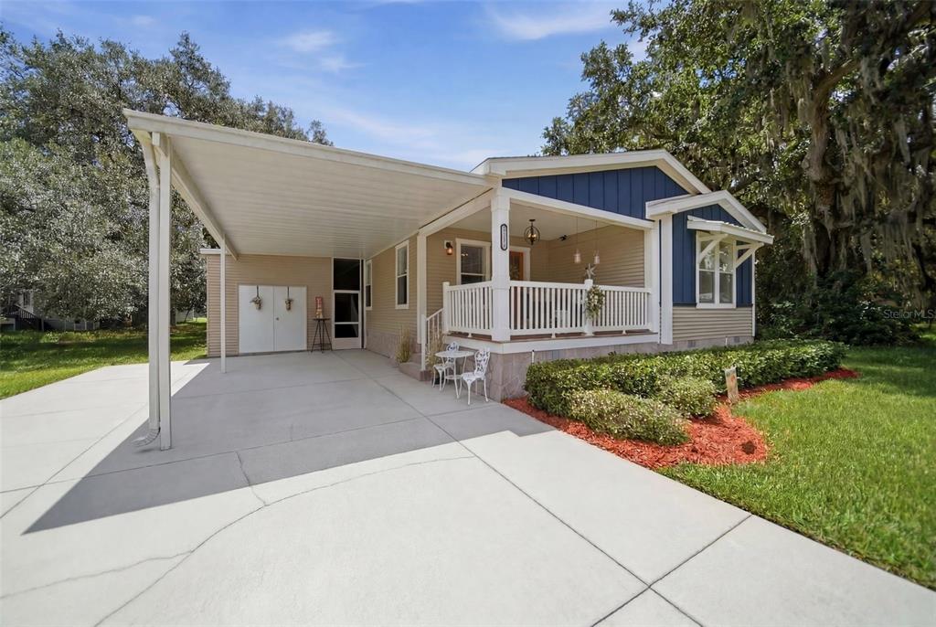 A single-story house features a covered carport, a front porch with white railings, and siding — 25138 BUTTONWOOD DRIVE, ASTATULA, FL