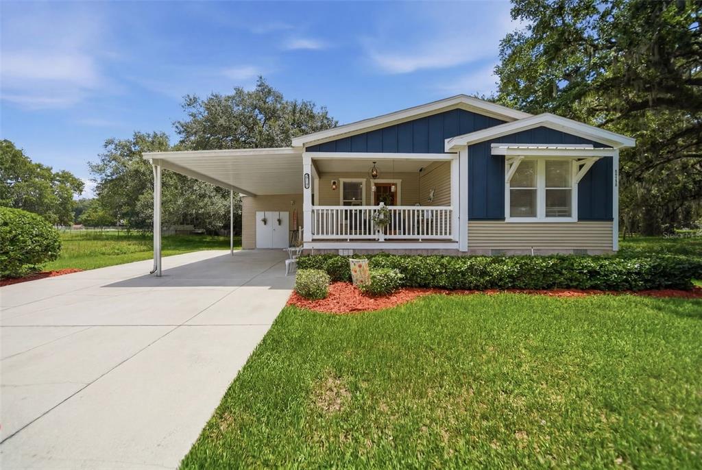 A single-story house with blue and tan siding, a front porch, and an attached carport — 25138 BUTTONWOOD DRIVE, ASTATULA, FL