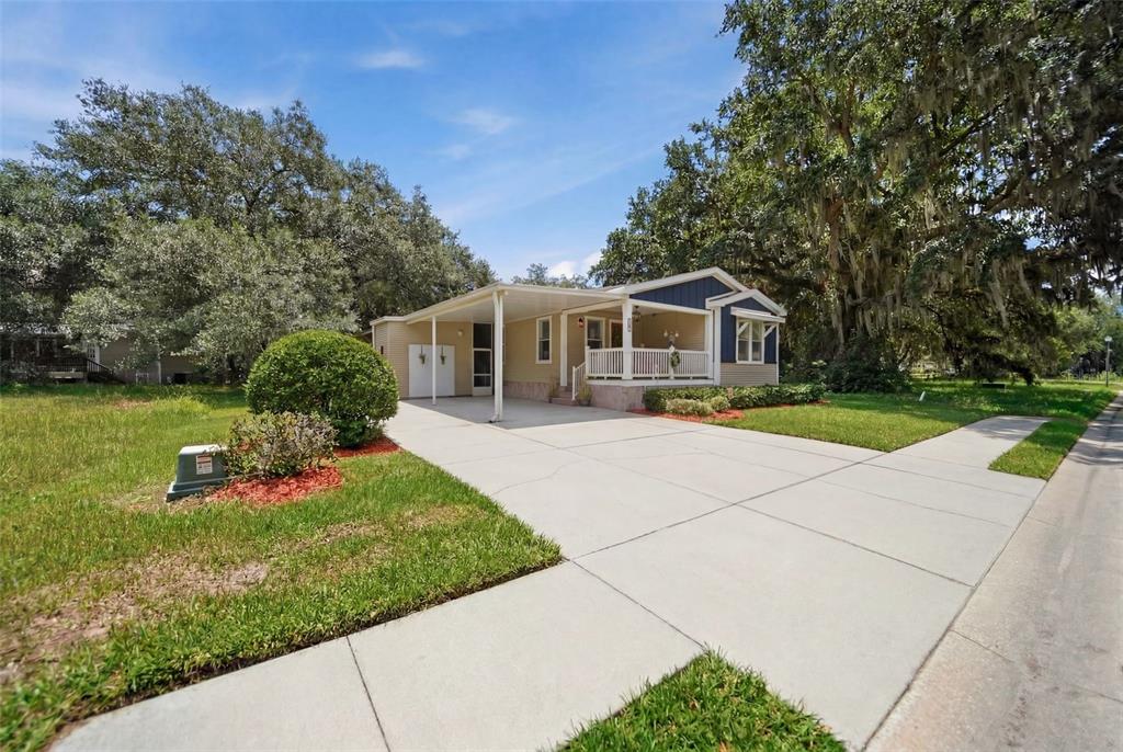 A single-story house with a carport, front porch, and large oak trees in the yard — 25138 BUTTONWOOD DRIVE, ASTATULA, FL