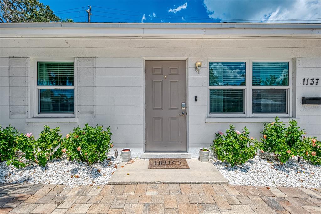 The exterior of a white house features a gray front door and a paved walkway — 1137 N MOONMIST COURT UNIT L-7, SARASOTA, FL