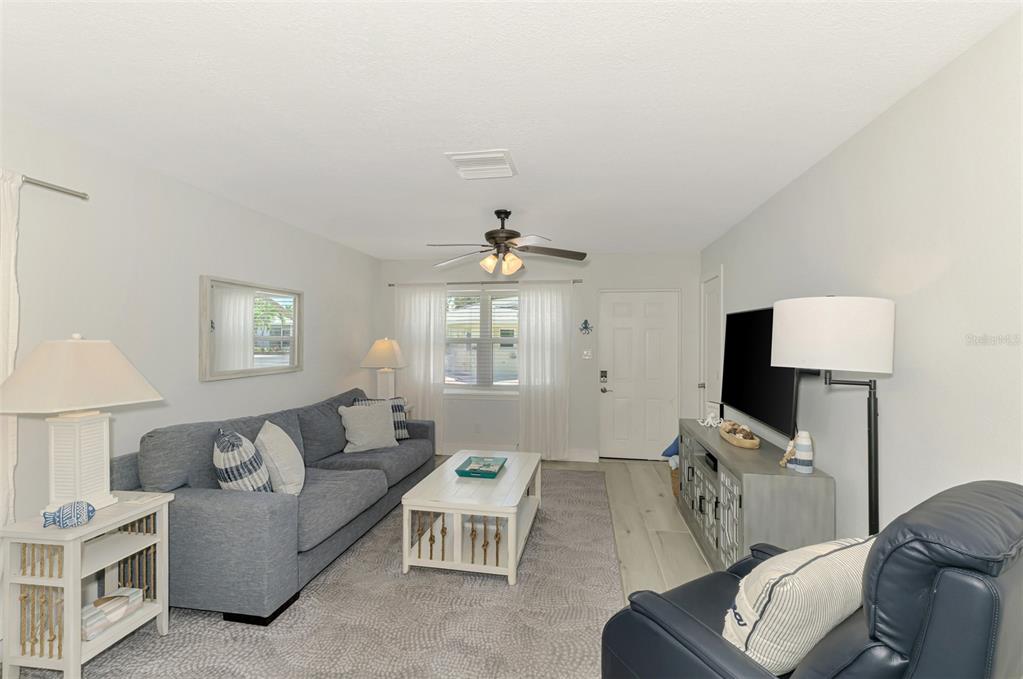 A living room features a gray sofa, a white coffee table, and a television console — 1137 N MOONMIST COURT UNIT L-7, SARASOTA, FL