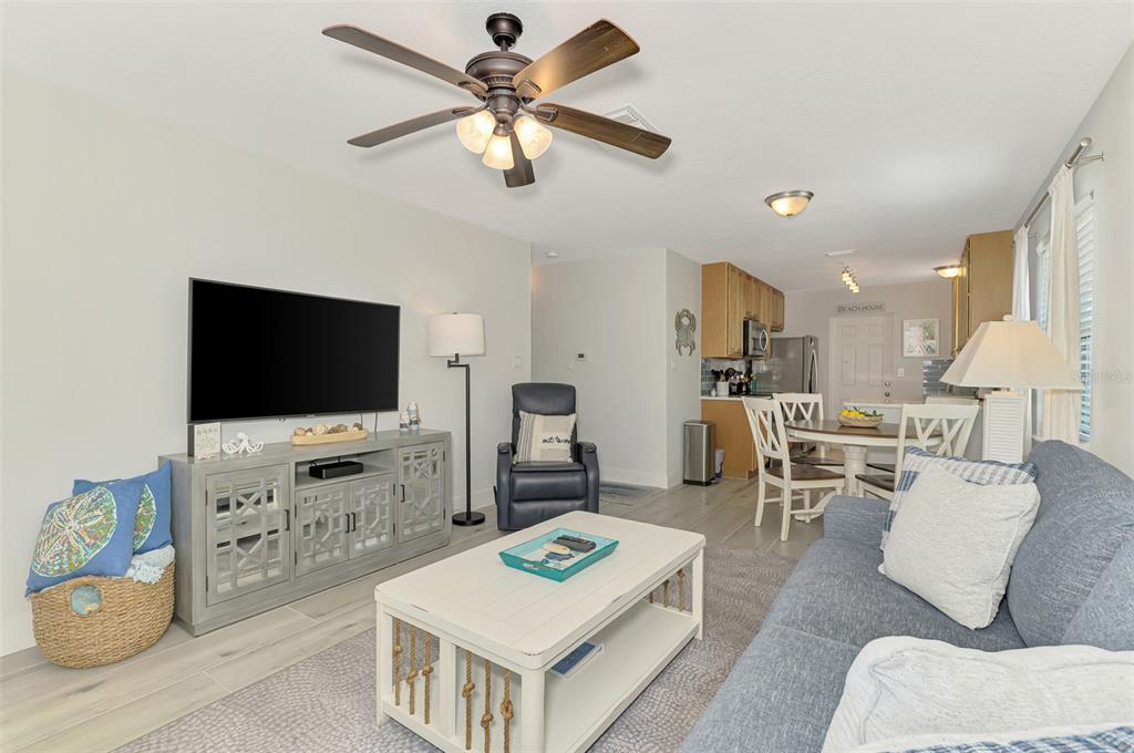 A living room with a gray sofa, coffee table, television console, and an adjacent dining area — 1137 N MOONMIST COURT UNIT L-7, SARASOTA, FL
