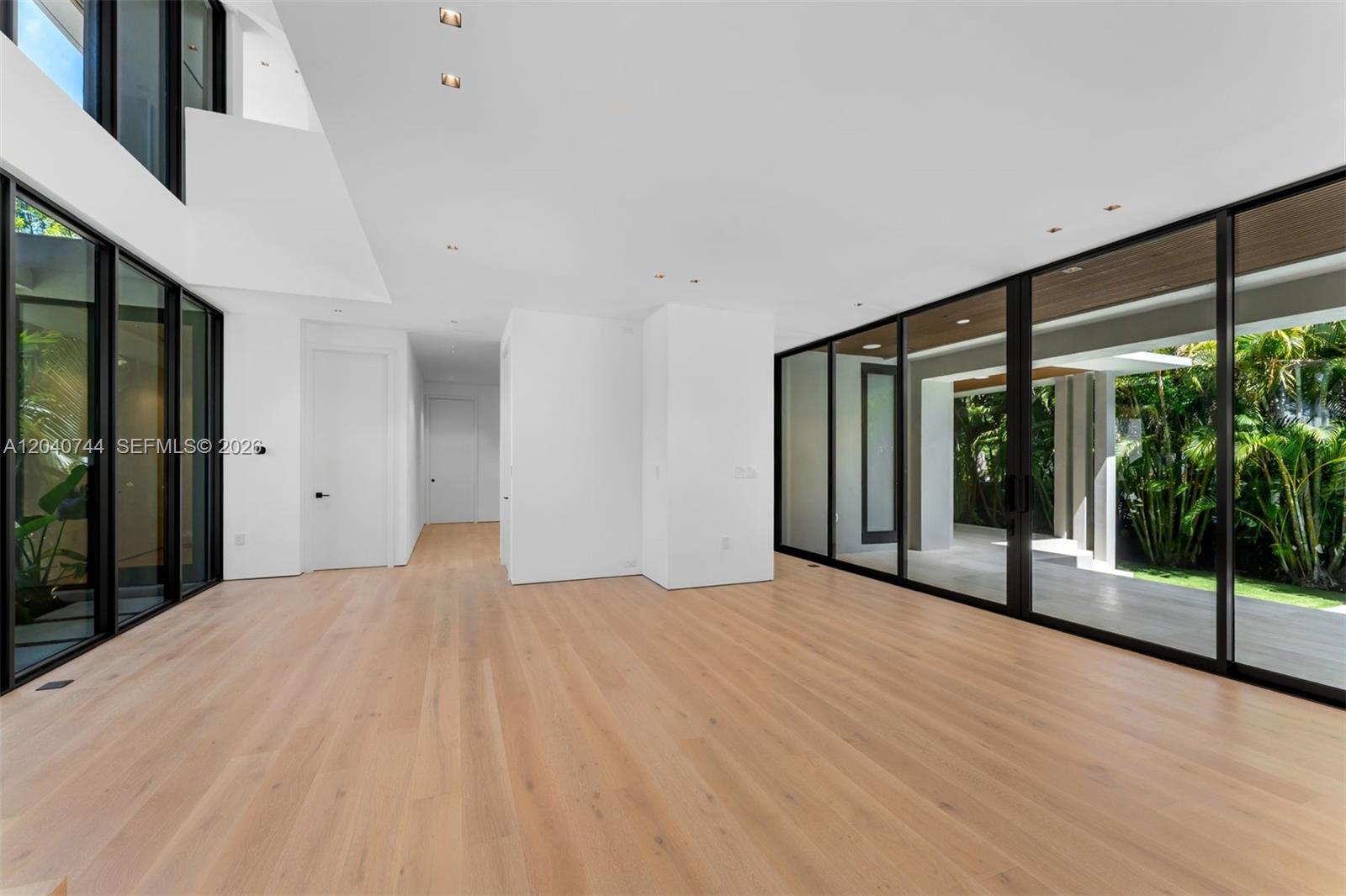 A bright, minimalist living space features light wood floors, white walls, and floor-to-ceiling glass walls — 165 Hampton Ln, Key Biscayne FL 33149, KEY BISCAYNE, FL