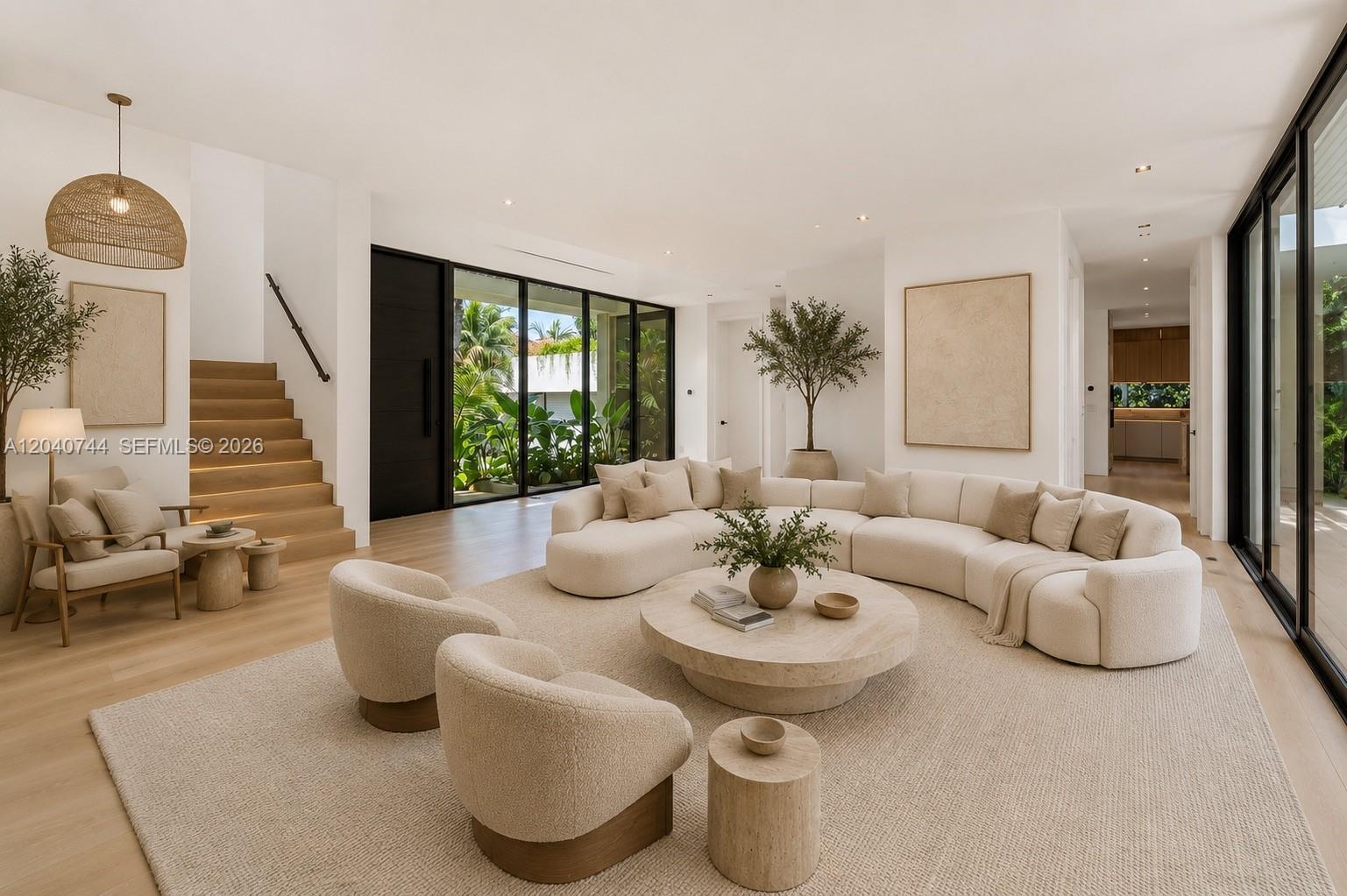 A modern living room features a curved sofa, neutral decor, light wood floors, and large windows — 165 Hampton Ln, Key Biscayne FL 33149, KEY BISCAYNE, FL