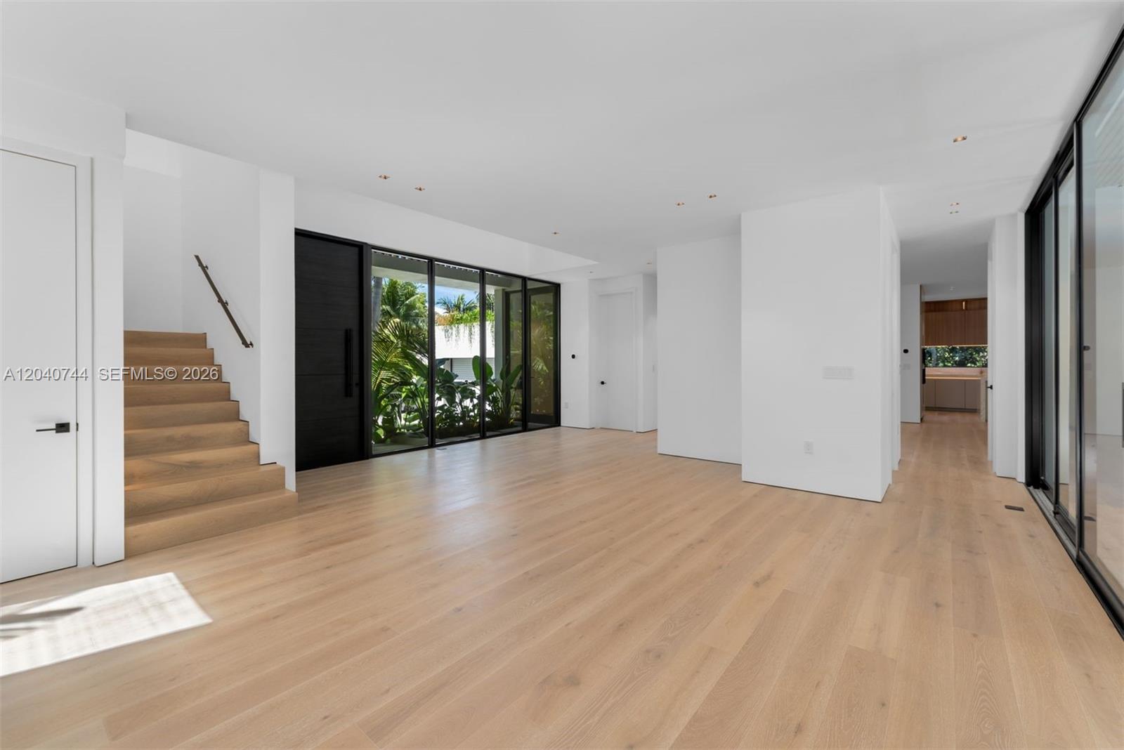 A minimalist living area features light wood flooring, a staircase, and floor-to-ceiling glass windows — 165 Hampton Ln, Key Biscayne FL 33149, KEY BISCAYNE, FL