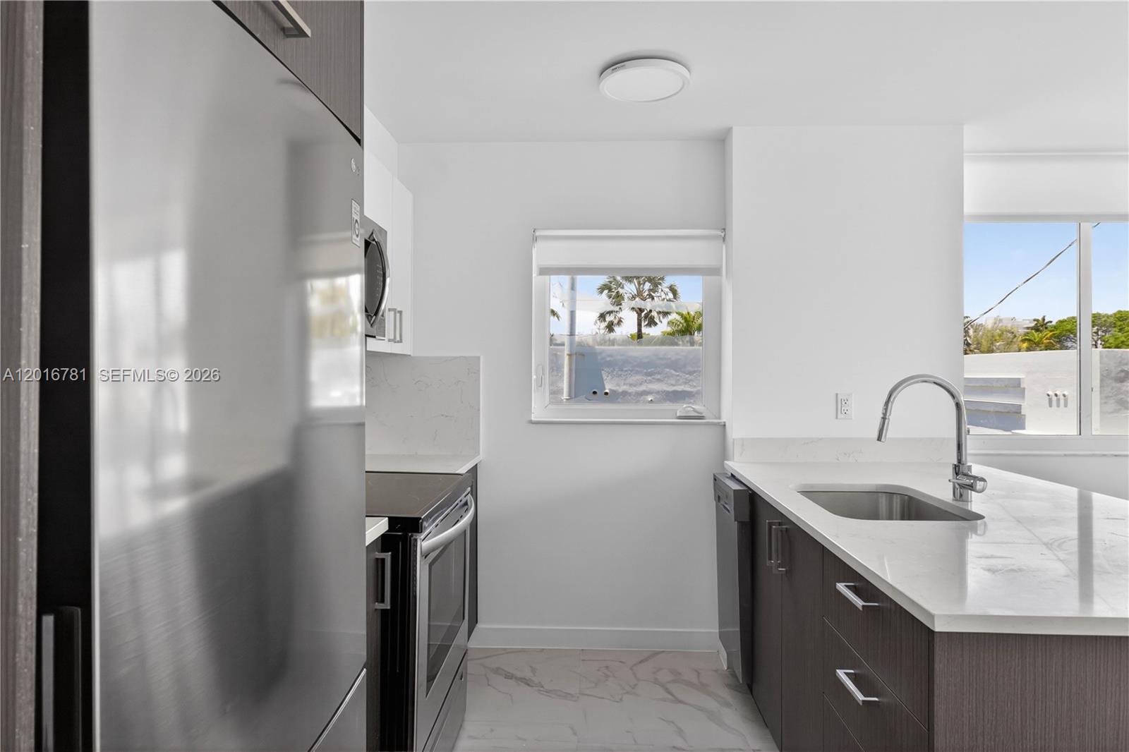 A modern kitchen features dark wood cabinets, white countertops, stainless steel appliances, and a window — 1552 Euclid Ave # 08, Miami Beach FL 33139, MIAMI BEACH, FL