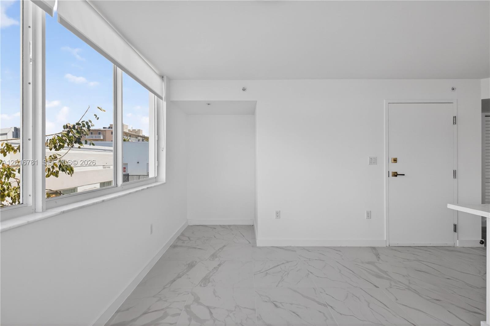 A bright, minimalist room features white walls, marble-patterned tile flooring, and a large window — 1552 Euclid Ave # 08, Miami Beach FL 33139, MIAMI BEACH, FL