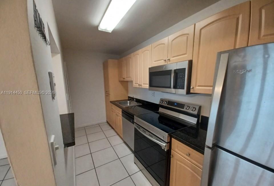 A galley-style kitchen features light wood cabinets, black countertops, and stainless steel appliances — 4330 NW 79th Ave # 2D, Doral FL 33166, DORAL, FL