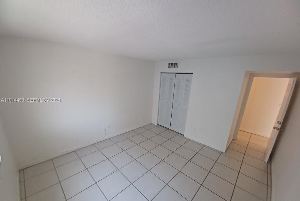An empty room features white walls, white tile flooring, a closet with louvered doors, and a doorway — 4330 NW 79th Ave # 2D, Doral FL 33166, DORAL, FL