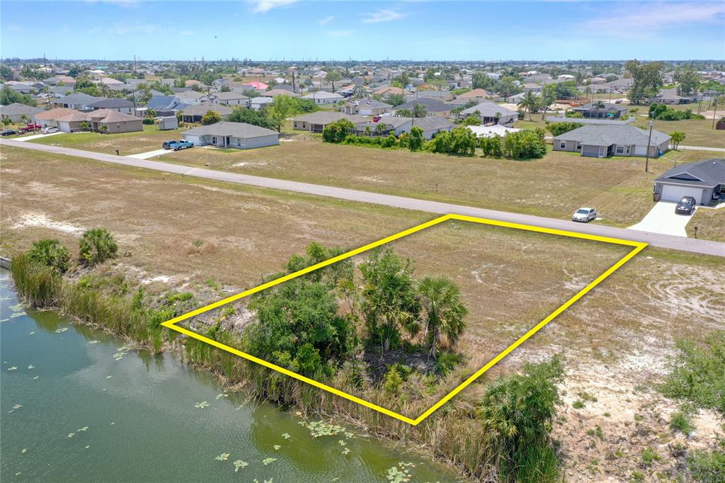 An aerial view shows a vacant, rectangular waterfront lot outlined in yellow near a road — 3023 NE 5TH PLACE, CAPE CORAL, FL
