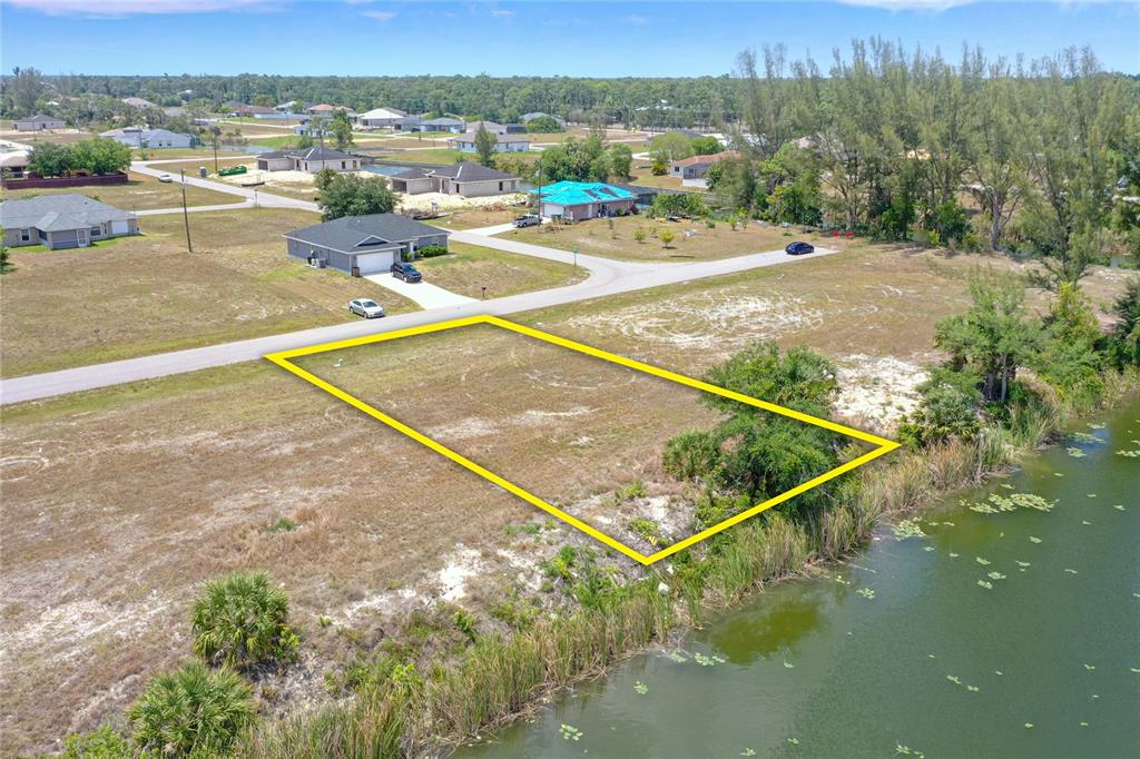 An aerial view shows a vacant, rectangular waterfront lot outlined in yellow near a road — 3023 NE 5TH PLACE, CAPE CORAL, FL