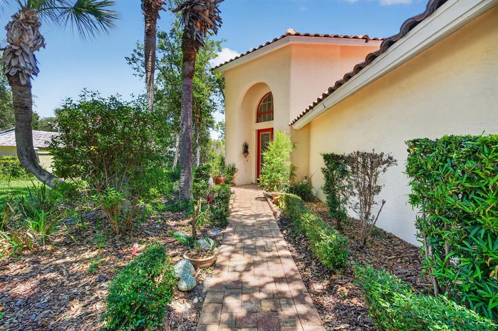 A brick walkway leads to the arched front entrance of a stucco house with landscaping — 10 MONTERREY DRIVE, PALM COAST, FL