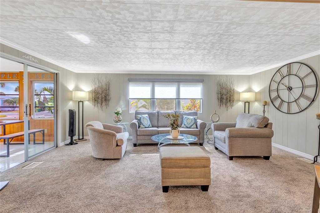 A living room with gray carpet, a sofa, two armchairs, and a large wall clock — 2100 KINGS HIGHWAY UNIT 289, PORT CHARLOTTE, FL