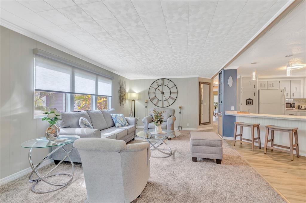A living room with gray carpet, a sofa, armchairs, and an open kitchen with bar seating — 2100 KINGS HIGHWAY UNIT 289, PORT CHARLOTTE, FL