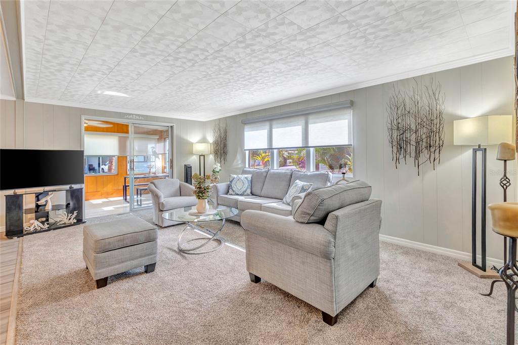 A living room features gray carpet, light-colored walls, a sofa, armchairs, and a sliding glass door — 2100 KINGS HIGHWAY UNIT 289, PORT CHARLOTTE, FL