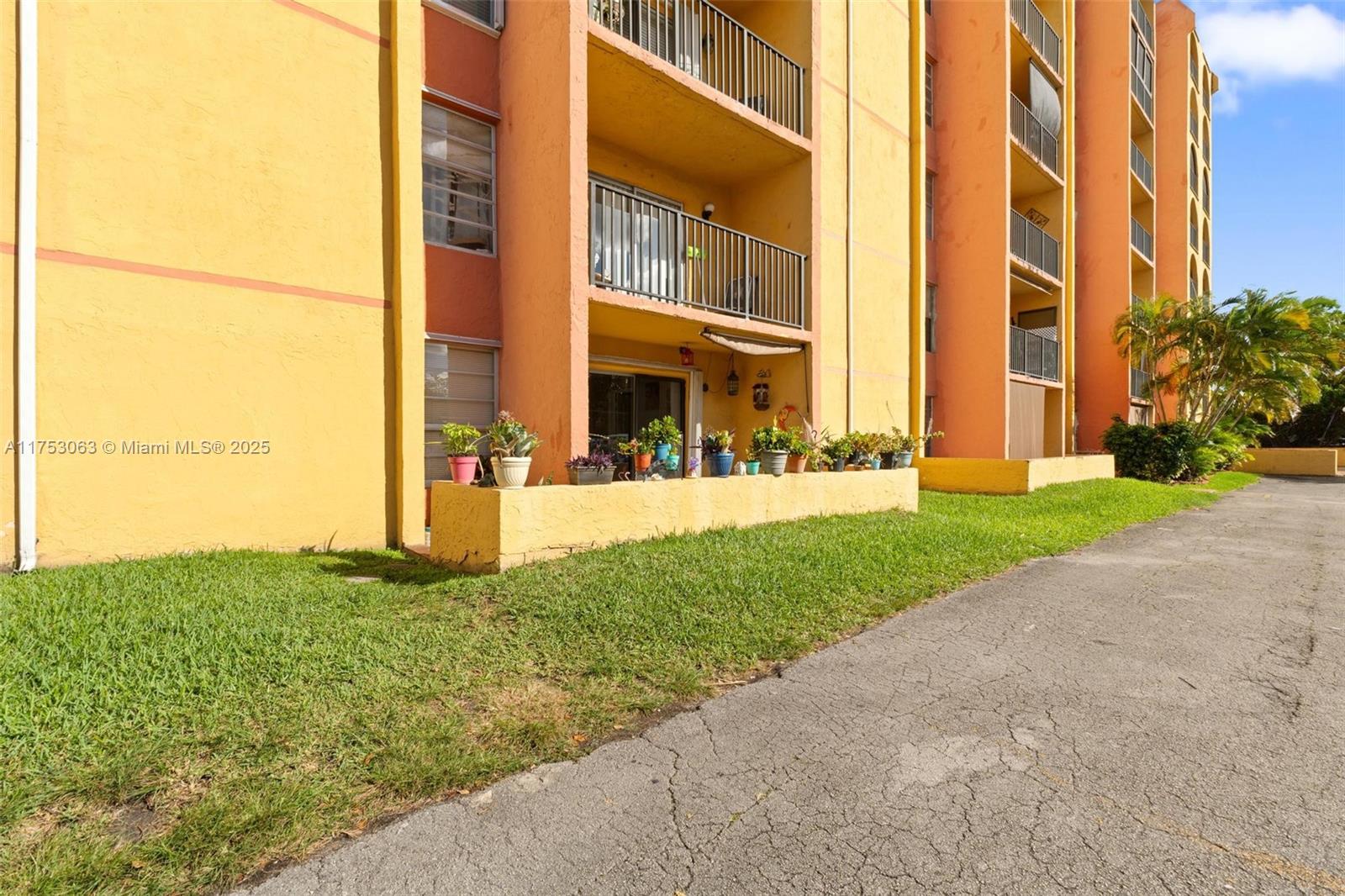 The exterior of a multi-story apartment building features yellow walls and private ground-floor patios — 4801 NW 7th St # 16, Miami FL 33126, MIAMI, FL