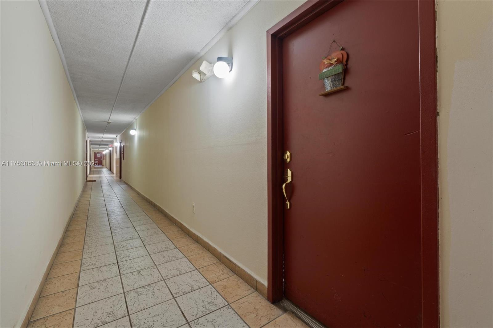 A long, tiled indoor hallway features a red door with a welcome sign — 4801 NW 7th St # 16, Miami FL 33126, MIAMI, FL