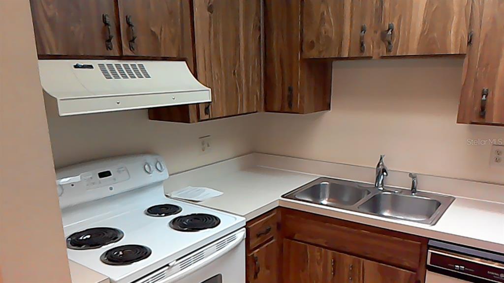 A kitchen features wood cabinets, a white electric stove, and a double-basin stainless steel sink — 706 GREEN VALLEY ROAD UNIT E4, PALM HARBOR, FL