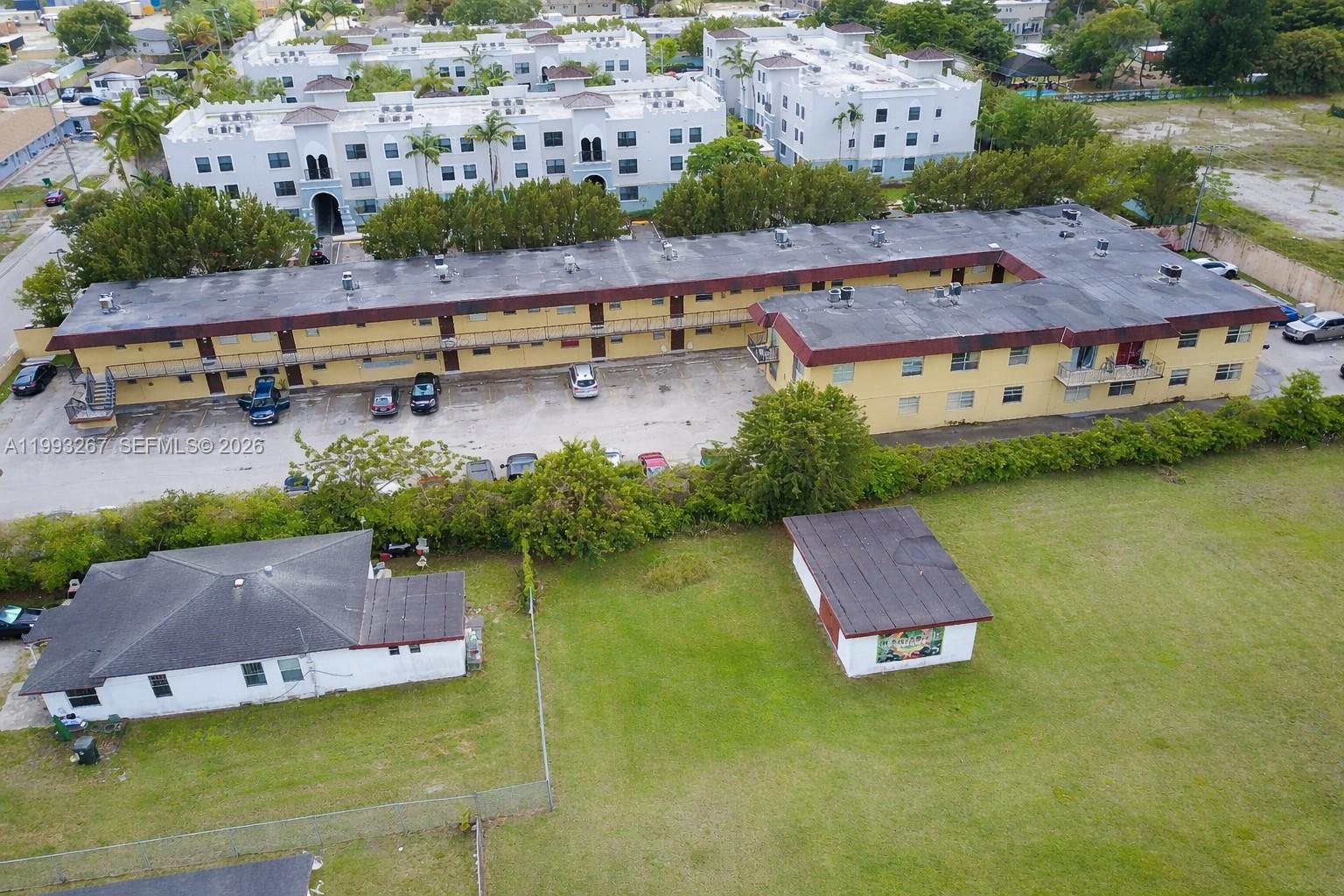This aerial view shows an L-shaped building with a parking lot and surrounding properties — 13380 Port Said Rd, Opa-Locka FL 33054, OPA-LOCKA, FL