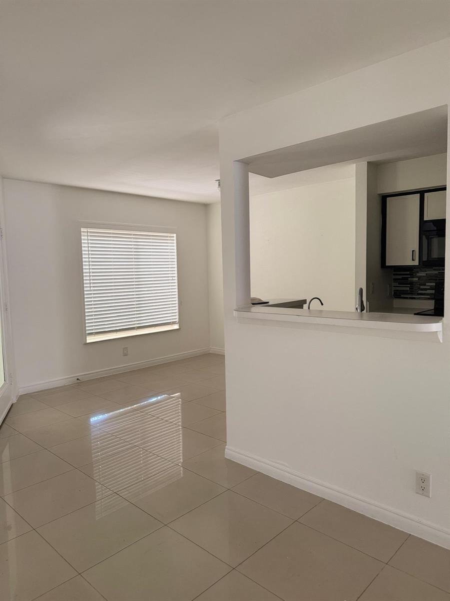 A room with light-colored tile flooring features a window with blinds and a kitchen pass-through — 815 West Boynton Beach Boulevard # 103, Boynton Beach FL 33426, BOYNTON BEACH, FL