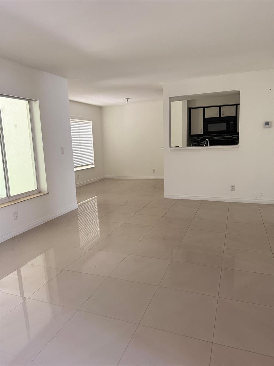 An open-concept living area with light-colored tile flooring and a kitchen pass-through window — 815 West Boynton Beach Boulevard # 103, Boynton Beach FL 33426, BOYNTON BEACH, FL