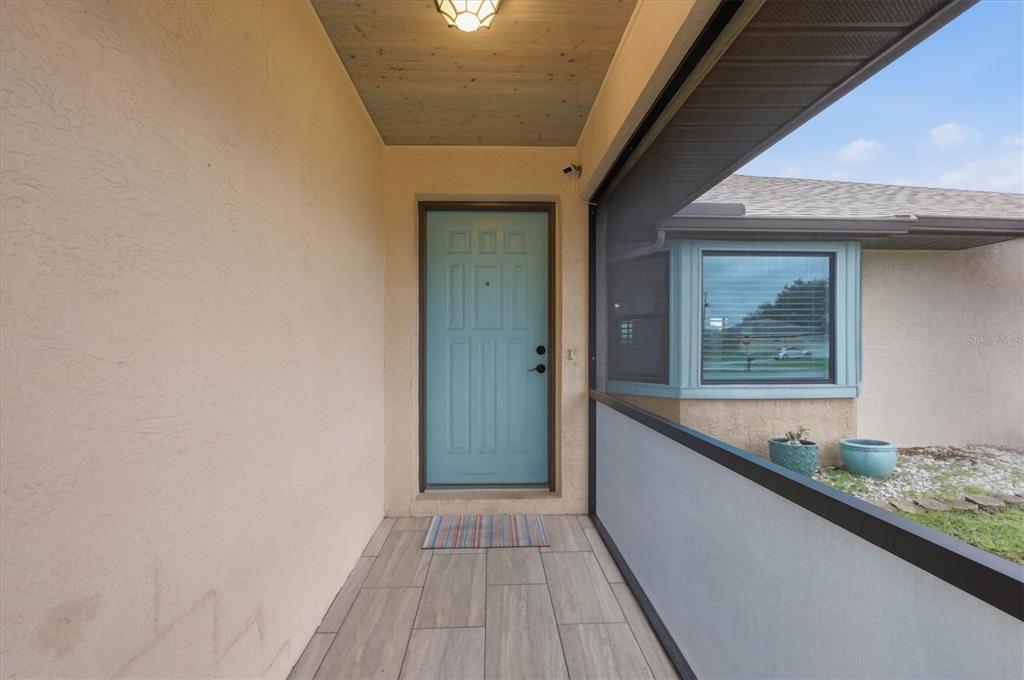 A covered entryway features a light blue front door, wood-look tile flooring, and a screened enclosure — 2671 YUCCA ROAD, VENICE, FL