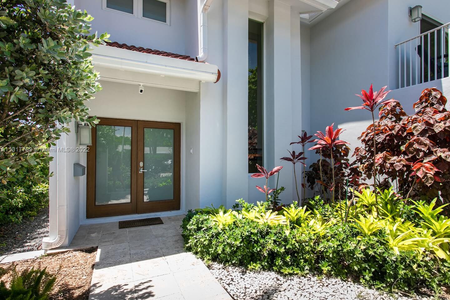 A white house exterior features a double glass door entrance and lush tropical landscaping — 1022 Adams St, Hollywood FL 33019, HOLLYWOOD, FL