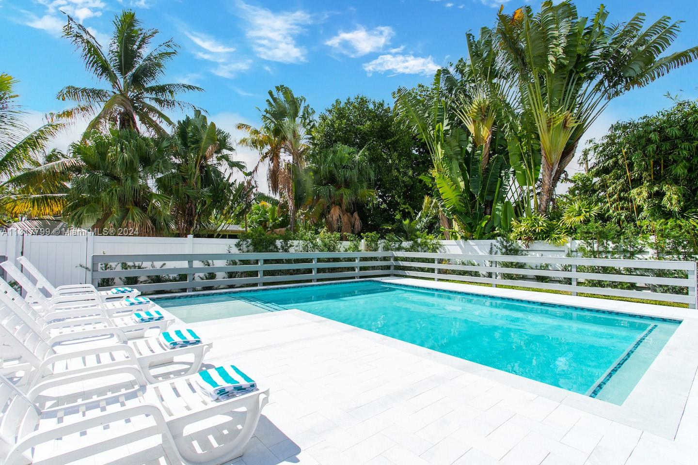 A rectangular swimming pool with white lounge chairs sits on a patio surrounded by palm trees — 1022 Adams St, Hollywood FL 33019, HOLLYWOOD, FL