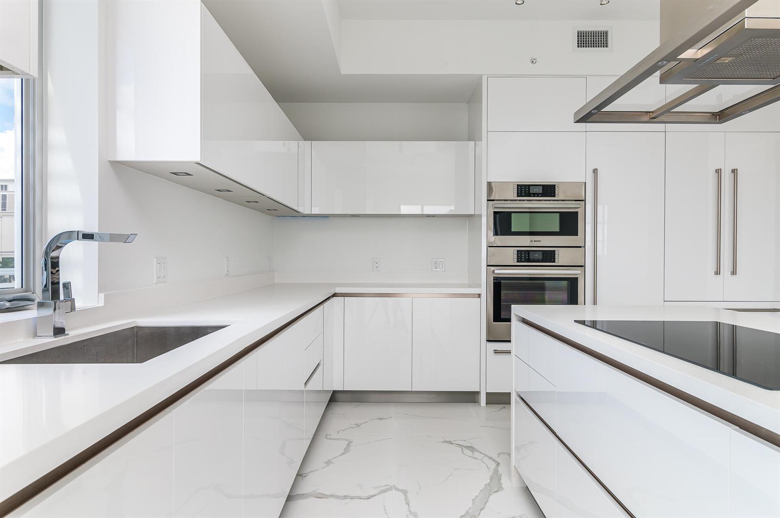 A modern white kitchen features glossy cabinets, marble-patterned flooring, and stainless steel built-in appliances — 155 E Boca Raton Road # 603, Boca Raton FL 33432, BOCA RATON, FL