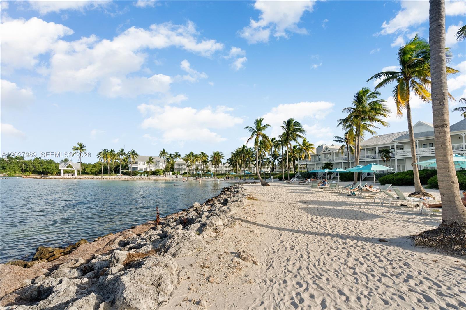 A sandy beach with lounge chairs and palm trees sits beside a calm bay — 2600 Overseas Hwy # 85, Marathon FL 33050, MARATHON, FL