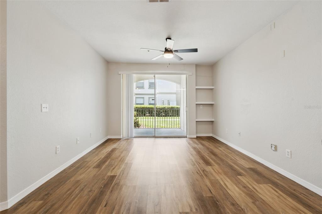 An empty living room with wood-look flooring, a ceiling fan, built-in shelves, and sliding doors — 2603 MAITLAND CROSSROAD UNIT 104, ORLANDO, FL