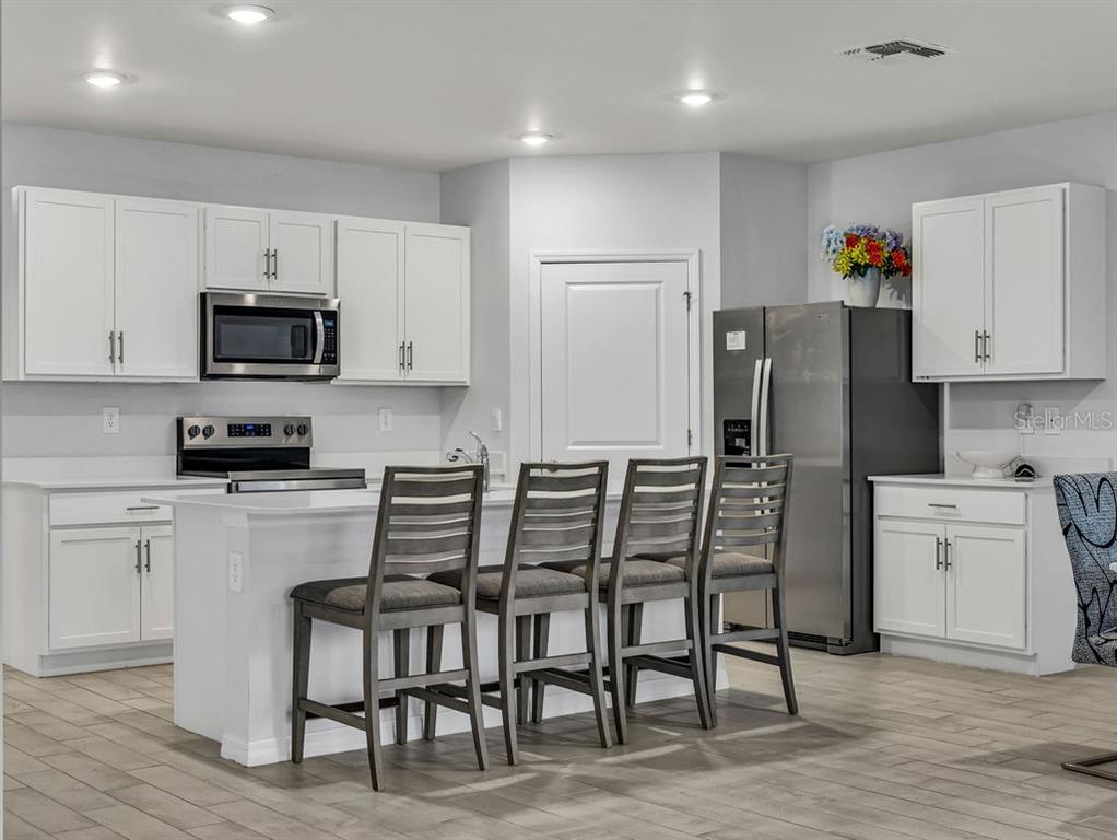A kitchen features white cabinets, stainless steel appliances, a center island, and four bar stools — 1048 ADALIA TERRACE, PORT CHARLOTTE, FL