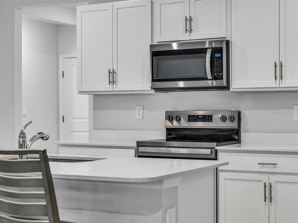 A modern kitchen features white cabinets, stainless steel appliances, and a white quartz island countertop — 1048 ADALIA TERRACE, PORT CHARLOTTE, FL