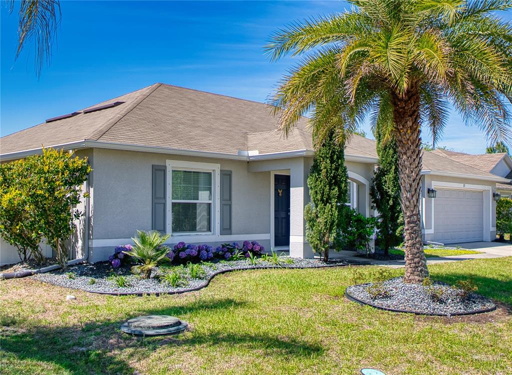 A single-story house with a palm tree, landscaped garden, and a garage under a blue sky — 27 LEWISDALE LANE, PALM COAST, FL