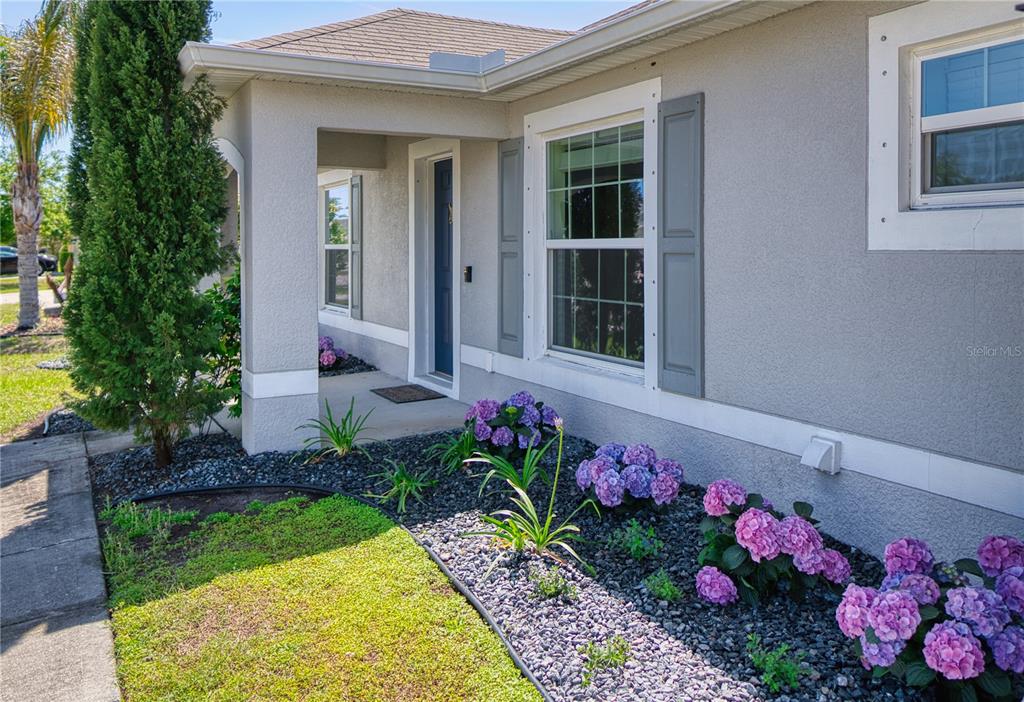 The exterior of a house features a covered entryway, gray stucco walls, and hydrangea bushes — 27 LEWISDALE LANE, PALM COAST, FL
