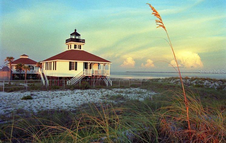 Two white stilt houses with red roofs stand on a sandy beach near the ocean — 115 BEAU RIVAGE DRIVE, ROTONDA WEST, FL
