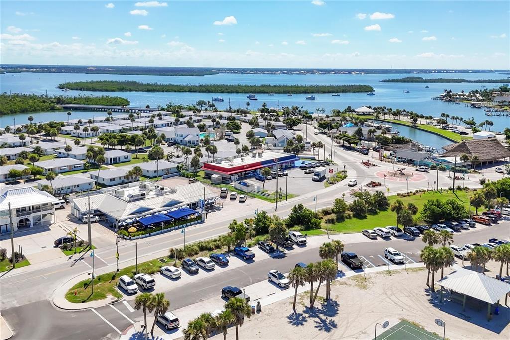 An aerial view shows a coastal community with a restaurant, parking lots, and nearby water — 115 BEAU RIVAGE DRIVE, ROTONDA WEST, FL