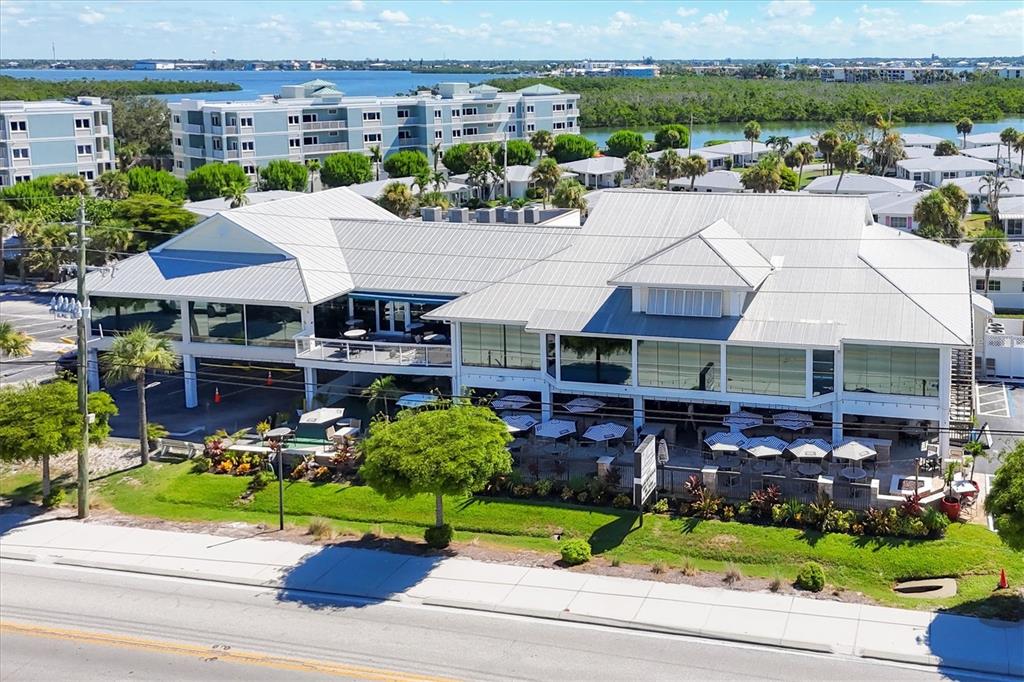 An aerial view shows a large, multi-level commercial building with a metal roof and patio — 115 BEAU RIVAGE DRIVE, ROTONDA WEST, FL