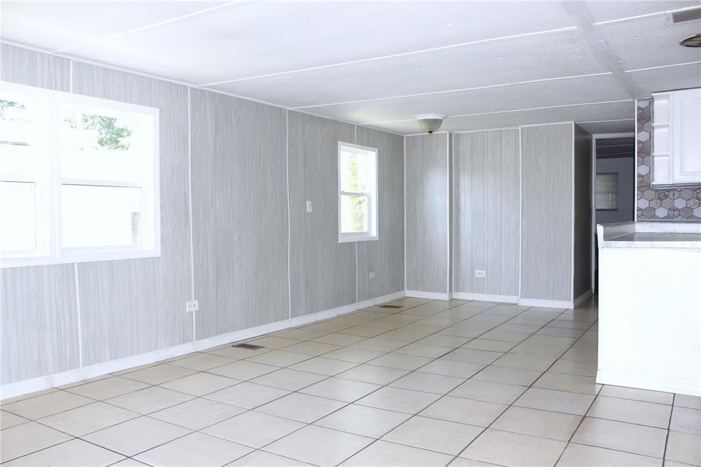 An empty room with light wood-paneled walls, white trim, and beige tiled flooring — 1845 DIXIE LANE, HOLIDAY, FL