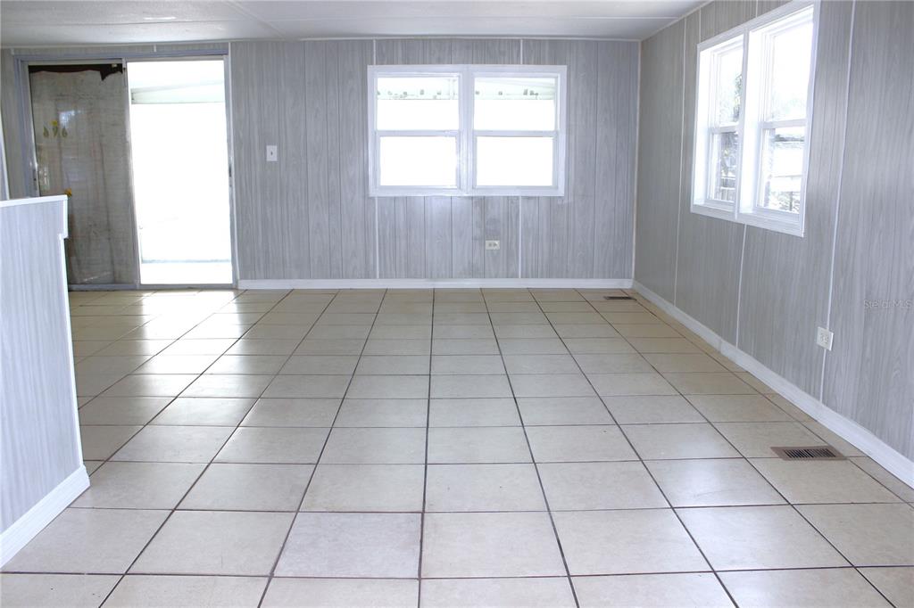 An empty room with light-colored tile flooring and gray wood-paneled walls — 1845 DIXIE LANE, HOLIDAY, FL